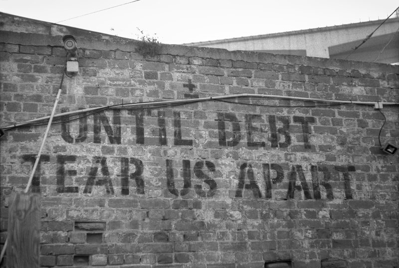 a sign on a brick wall that says until debt tears apart